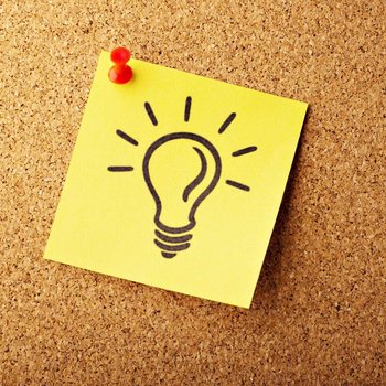 Ein gelber Zettel mit einer gemalten Glühbirne drauf hängt an einer Pinnwand.